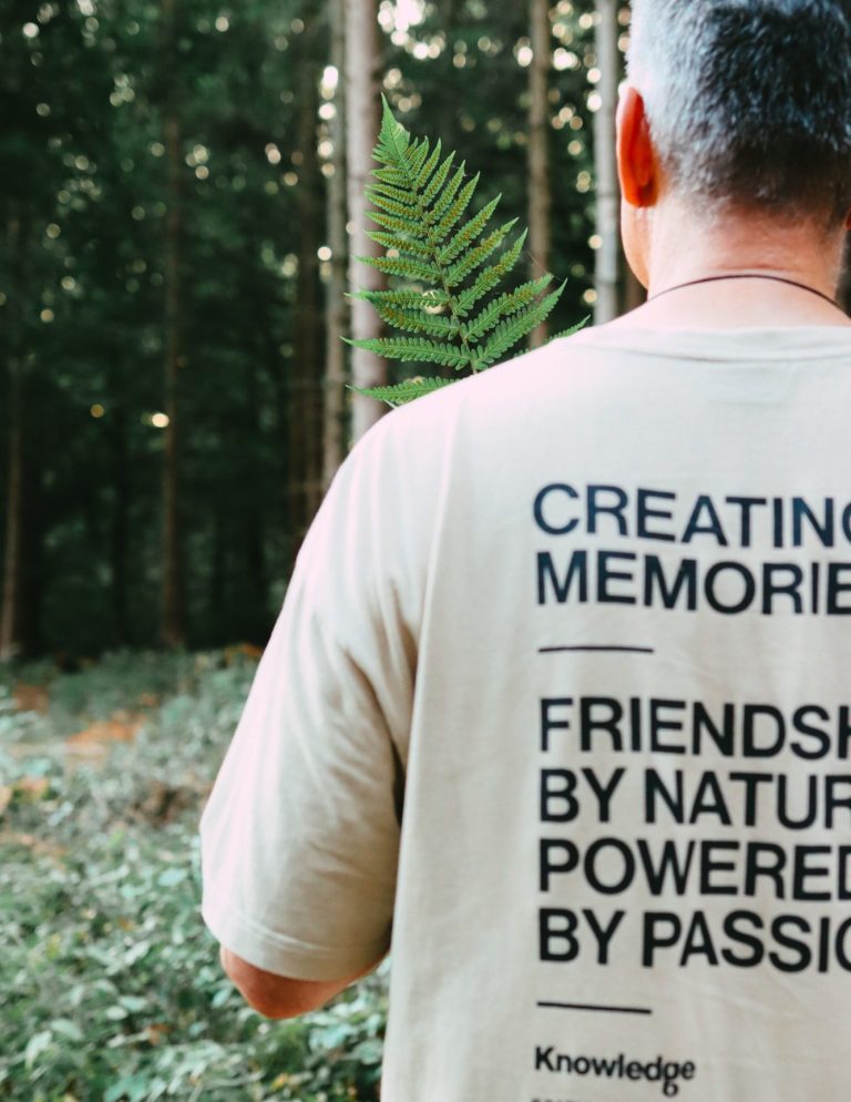 Hinteransicht einer Person im Wald, die ein T-Shirt mit Motiv über Freundschaft und Erinnerungen trägt.