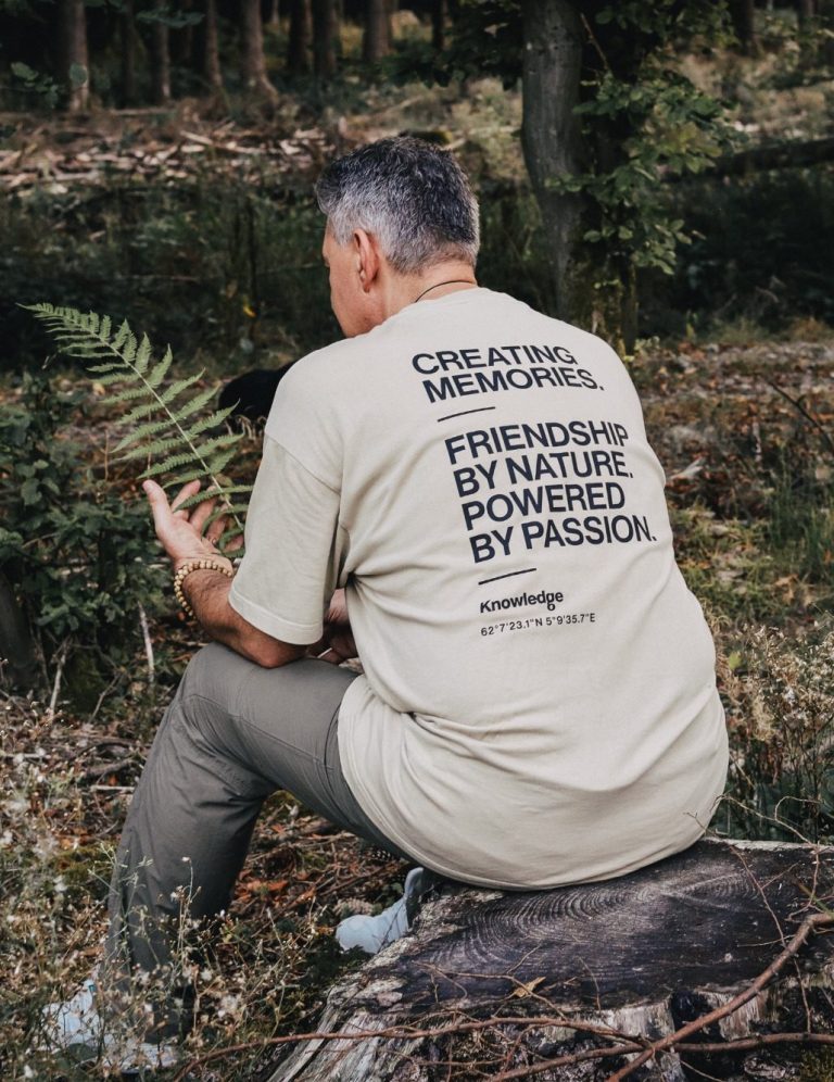 Mann sitzt auf Baumstamm, trägt T-Shirt mit Text zur Umwelt und Leidenschaft.